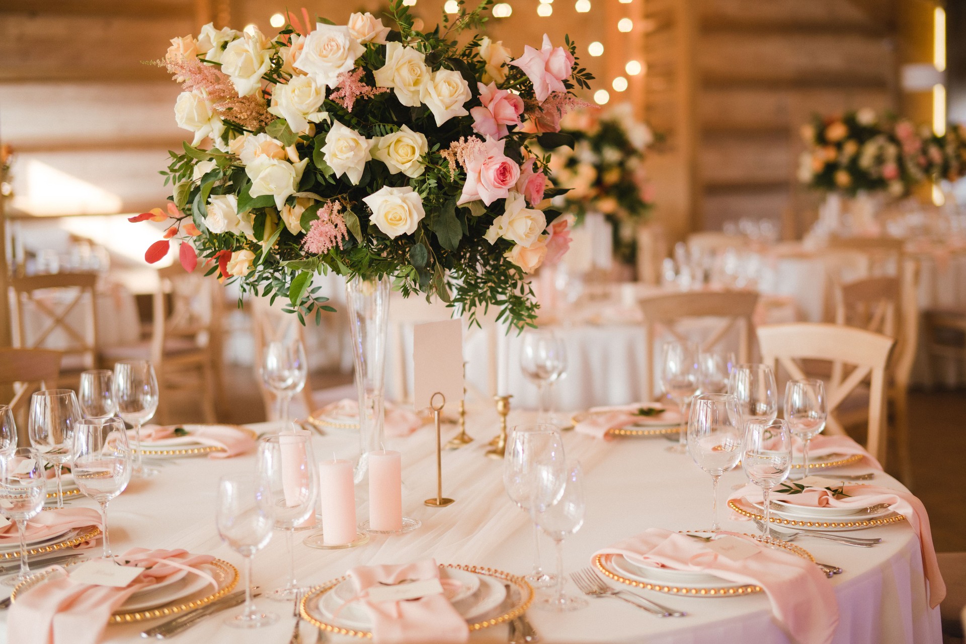 Table setting at the wedding reception. Floral compositions with beautiful flowers and greenery, candles, laying and plates on a decorated table.